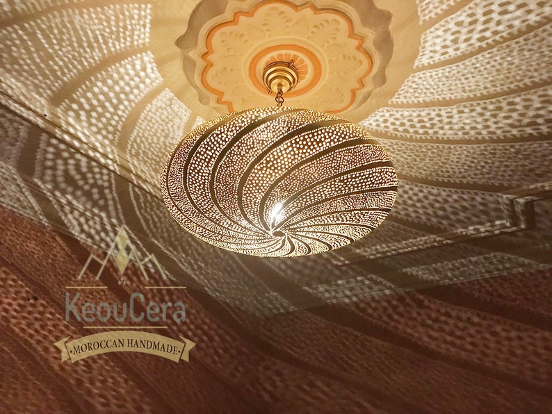 May include: A gold Moroccan pendant light with a geometric pattern. The light casts intricate shadows on the ceiling.