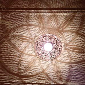 May include: A round, metal Moroccan pendant light fixture with a geometric design. The light is on and casting a patterned shadow on the ceiling.