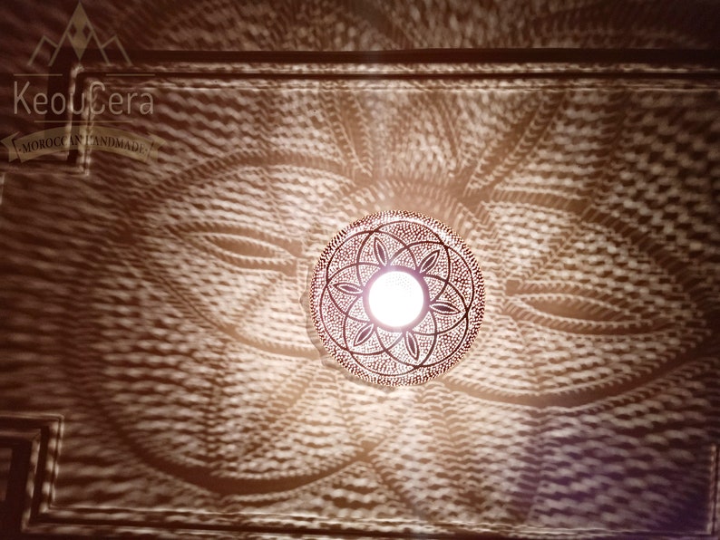 May include: A round, metal Moroccan pendant light fixture with a geometric design. The light is on and casting a patterned shadow on the ceiling.