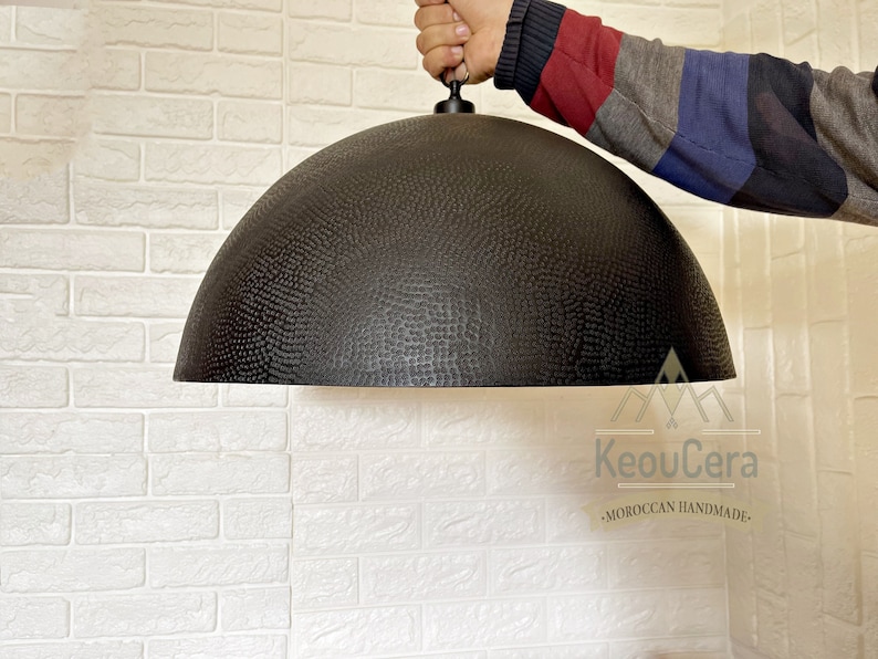 May include: A black, hammered metal dome pendant light fixture hanging from a ceiling. The light fixture has a textured surface and is suspended by a black cord.