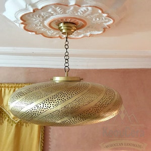 May include: A gold-colored, round, hanging light fixture with a decorative, perforated pattern. The light fixture is suspended from a chain and has a decorative, ornate ceiling fixture.