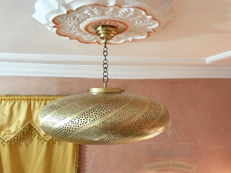 May include: A gold-colored, round, hanging light fixture with a decorative, perforated pattern. The light fixture is suspended from a chain and has a decorative, ornate ceiling fixture.