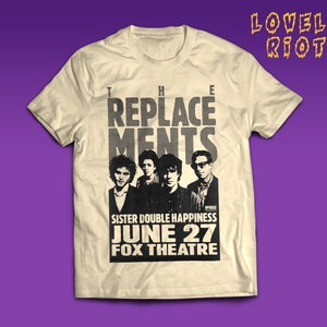 Puede incluir: Una camiseta beige con un estampado gráfico en blanco y negro de la banda "The Replacements". El gráfico incluye el nombre de la banda, la fecha "June 27" y el lugar "Fox Theatre".