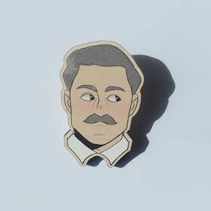 May include: Wooden pin depicting a cartoon illustration of a man's face with a grey moustache and hair, wearing a white collared shirt. The pin has a light brown border on a white background.