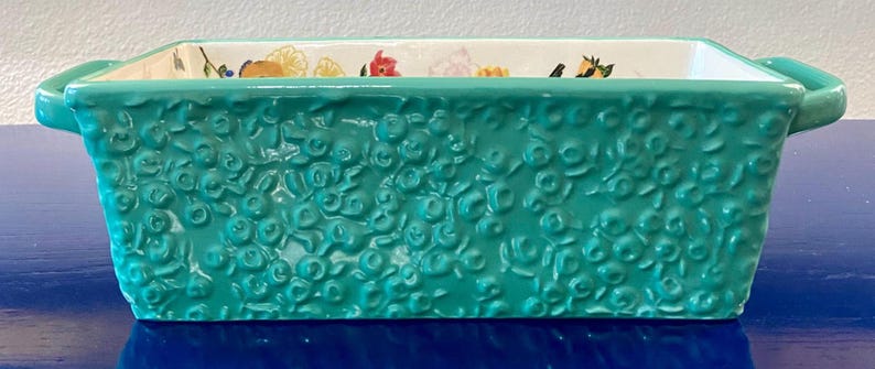 K&ouml;nnte beinhalten: Eine rechteckige t&uuml;rkisfarbene Keramik-Backform mit gepr&auml;gten floralen Details. Die Form hat zwei Griffe und ein Blumenmuster am Innenrand. Dieser K&uuml;chenartikel eignet sich zum Backen und Servieren.