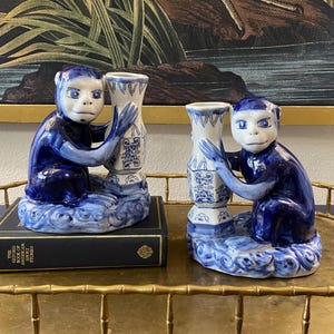 May include: A pair of blue and white porcelain monkey candle holders. Each monkey is holding a vase with a blue and white floral design. The vases are sitting on a cloud-shaped base.