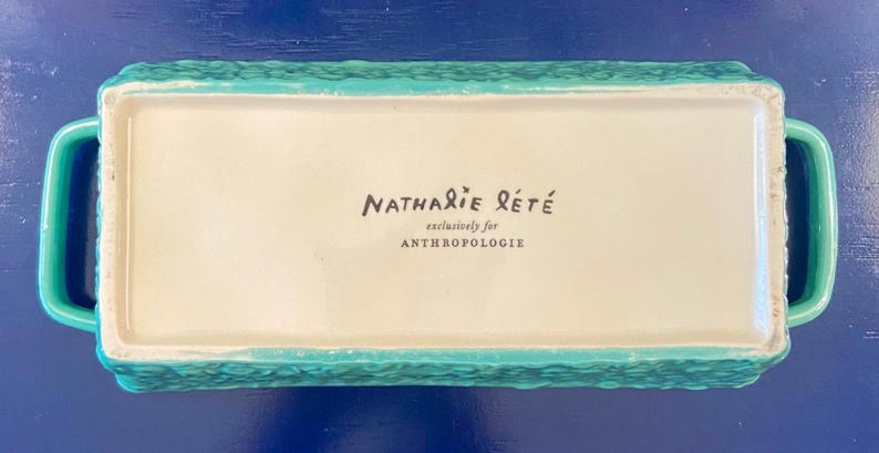 K&ouml;nnte beinhalten: Rechteckige t&uuml;rkisfarbene Keramikschale mit Griffen. Die Schale hat eine strukturierte Au&szlig;enseite und eine cremefarbene Innenseite. Der Text "Nathalie Lete exclusively for Anthropologie" ist innen aufgedruckt.