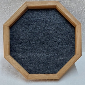 May include: Octagonal wooden frame with a dark gray felt insert. The frame is made of light brown wood and has a beveled edge.