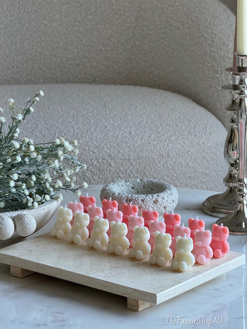 May include: A collection of small, bear-shaped candles in alternating shades of cream and soft pink, arranged in rows on a rectangular stone tray. Each candle features a simple wick at the top. The text TheFavourShopAU is visible in the bottom right.