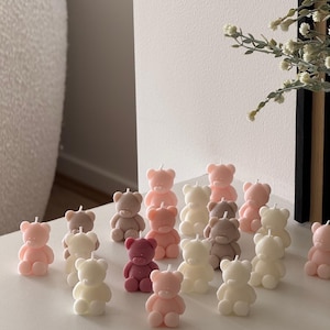May include: A collection of small, bear-shaped candles in various pastel shades including soft pink, cream, white, and muted brown. Each candle features a simple, molded bear design with a single wick on top. The text TheFavourShopAU is visible.