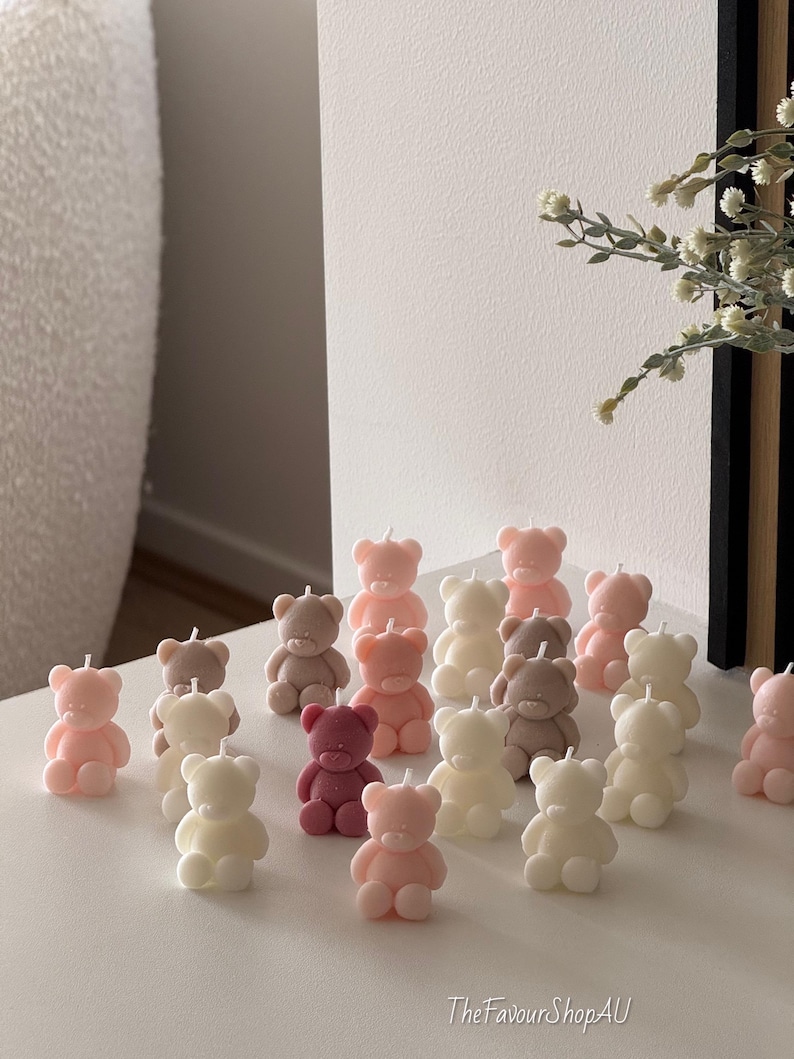 May include: A collection of small, bear-shaped candles in various pastel shades including soft pink, cream, white, and muted brown. Each candle features a simple, molded bear design with a single wick on top. The text TheFavourShopAU is visible.