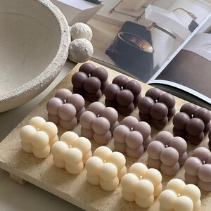 May include: A selection of bubble-shaped candles in cream, pale pink, and brown hues, displayed on a rectangular stone tray. The candles feature a smooth, spherical design. The FavourShopAU is printed on the bottom right.