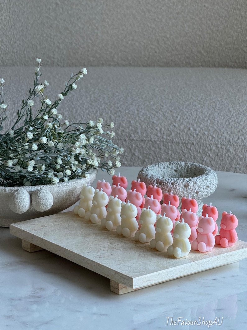 May include: A collection of small, bear-shaped candles in shades of cream and soft pink, arranged in rows on a rectangular stone tray. The candles feature a simple wick at the top. The text TheFavourShopAU is visible in the bottom right corner.