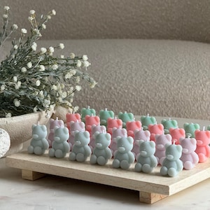 May include: A collection of small, bear-shaped candles in pastel pink, light blue, and sage green arranged in rows on a rectangular stone tray. Each candle features a single white wick at the top. The text TheFavourShopAU is visible at the bottom.