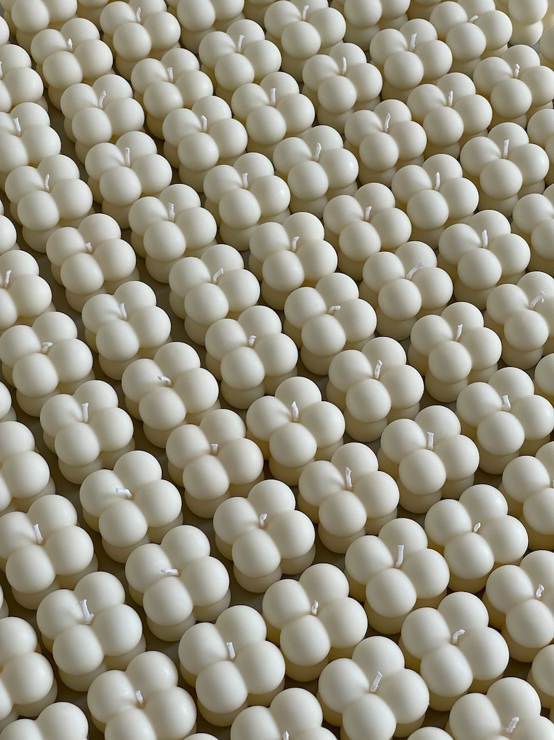 May include: A top-down view of many ivory bubble candles, neatly aligned. Each candle features four spheres and a central white wick. The candles have a smooth, matte surface, giving a consistent, soft look. The arrangement suggests a collection of decorative items.
