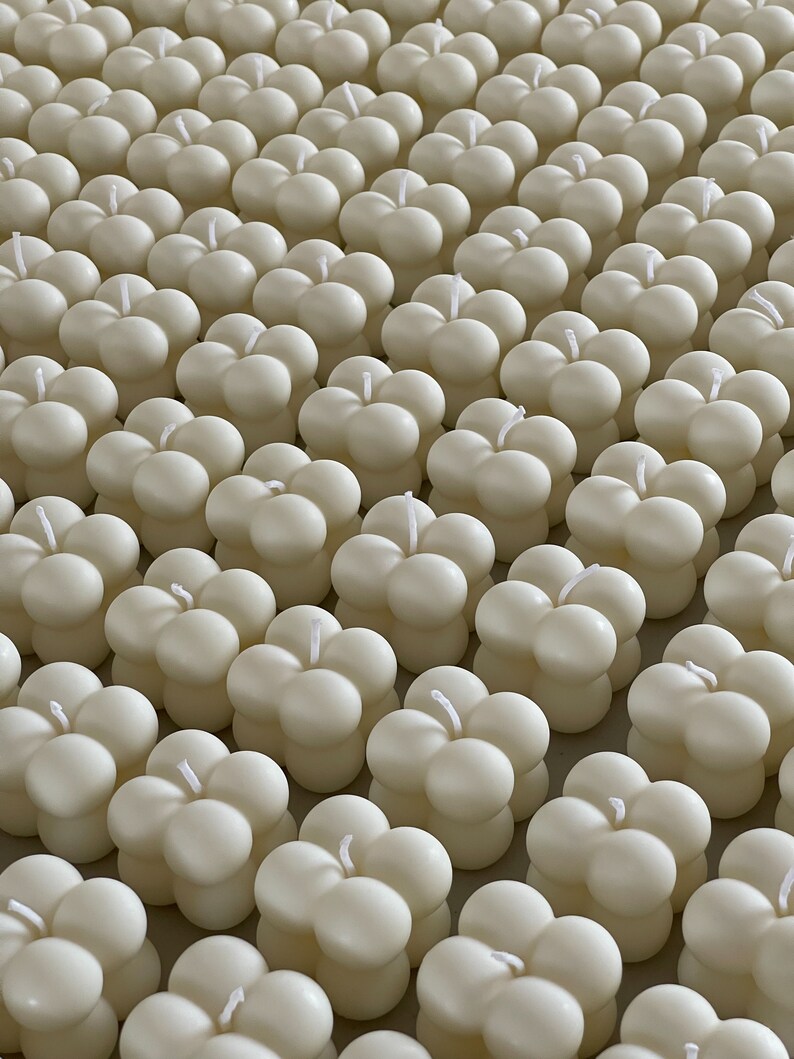 May include: A close-up of many ivory-coloured bubble candles. Each candle has a spherical shape with four rounded sections and a single wick. The candles are arranged in neat rows, creating a visually appealing pattern.