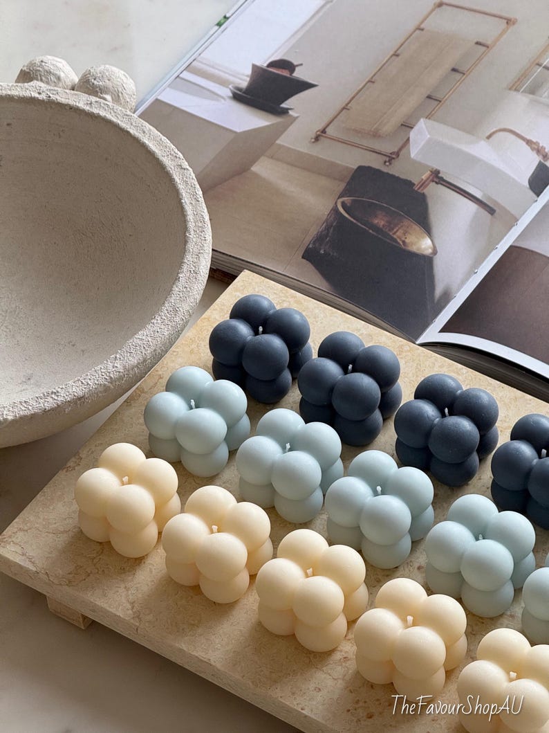 May include: A selection of bubble candles in shades of cream, pale blue, and navy blue, arranged on a light-toned rectangular tray. The candles are clustered together. The FavourShopAU is printed on the bottom right corner.