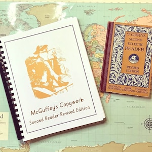 Może przedstawiać: Antyczna książka McGuffey's Second Reader Revised Edition w brązowej okładce z złotymi napisami. Książka jest otwarta na stronie z ilustracją osoby czytającej książkę. Książka leży na mapie świata.