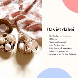 K&ouml;nnte beinhalten: Ein herzf&ouml;rmiger Eierkarton mit zwei gesprenkelten Eiern und einem wei&szlig;en Ei. Ein zweiter herzf&ouml;rmiger Beh&auml;lter mit einer Schleife befindet sich neben dem Karton. Der Text "Knack mich" steht auf einem kleinen runden Aufkleber.