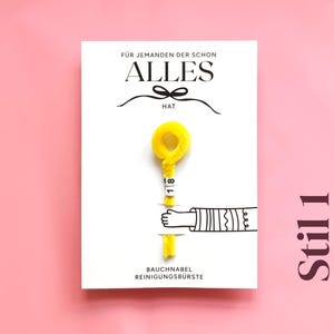 以下が含まれることがあります： 「ALLES」の文字と黄色の掃除ブラシが描かれた白いカード。カードには「F&Uuml;R JEMANDEN DER SCHON」と「BAUCHNABEL REINIGUNGSB&Uuml;RSTE」の文字が書かれています。背景は単色のピンク色です。