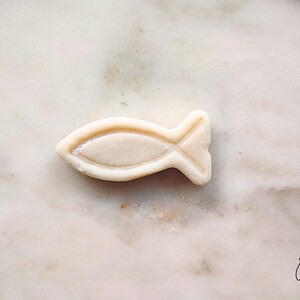 May include: A light-colored, fish-shaped object with a textured surface. The fish has a detailed fin and tail design. The object is set against a marble background.