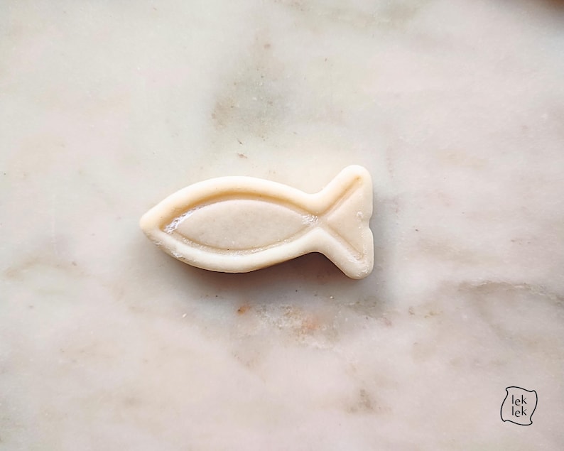 May include: A light-colored, fish-shaped object with a textured surface. The fish has a detailed fin and tail design. The object is set against a marble background.