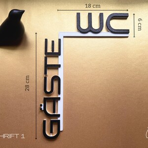 May include: A black decorative bird figurine next to a sign that reads "WC G&Auml;STE". The sign is 28 cm tall and 18 cm wide, with black letters on a white background. The sign is for a restroom.