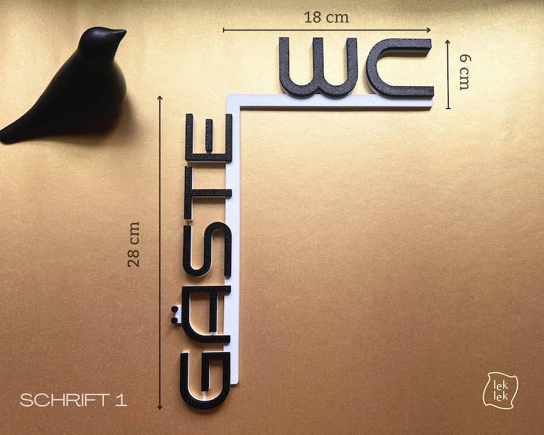 May include: A black decorative bird figurine next to a sign that reads "WC G&Auml;STE". The sign is 28 cm tall and 18 cm wide, with black letters on a white background. The sign is for a restroom.