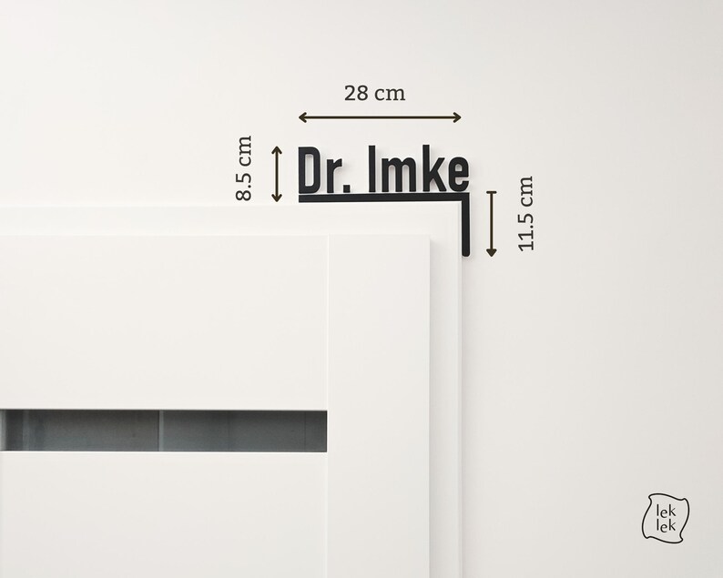 May include: Black metal sign that reads "Dr. Imke" with dimensions of 28 cm wide and 8.5 cm high. The sign is mounted on a corner piece that is 11.5 cm long. The sign is displayed on a white wall.