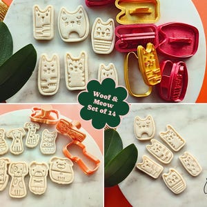 May include: A set of 14 cookie cutters in the shape of cats and dogs. The cutters are in various colors, including red, yellow, and orange. The cookies are beige and have detailed designs. The text "Woof & Meow Set of 14" is visible.