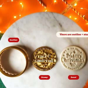 May include: A white ceramic cookie cutter with a scalloped edge and a gold-colored stamp with the text "A Joy  H21W  asmizing 26" on a white surface.  There is also a white ceramic cookie with the text "WE WISH YOU A Marry Christmas THE THOMPSONS" on it.