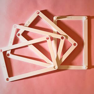 May include: A set of four white rectangular frames with rounded corners and circular holes at each corner. Each frame is marked with the text 1/8 inch, indicating specific measurements. The frames are arranged in a fanned, overlapping pattern.