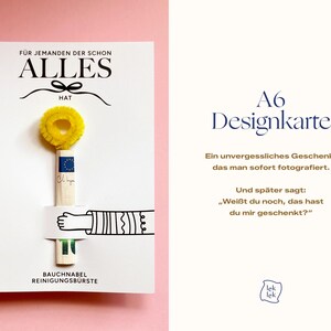 Op de afbeelding: Een witte rechthoekige kaart met de tekst F&Uuml;R JEMANDEN DER SCHON ALLES HAT en BAUCHNABEL REINIGUNGSB&Uuml;RSTE. Een gele pijpenrager is aan de kaart bevestigd, vastgehouden door een zwart-witte illustratie van een arm en een hand.