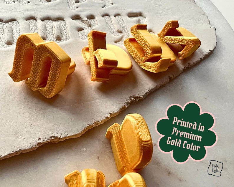 May include: A collection of three-dimensional gold-colored letters with a textured surface finish. A dark green scalloped badge features the white text Printed in Premium Gold Color. The letters are arranged on a light-colored surface.