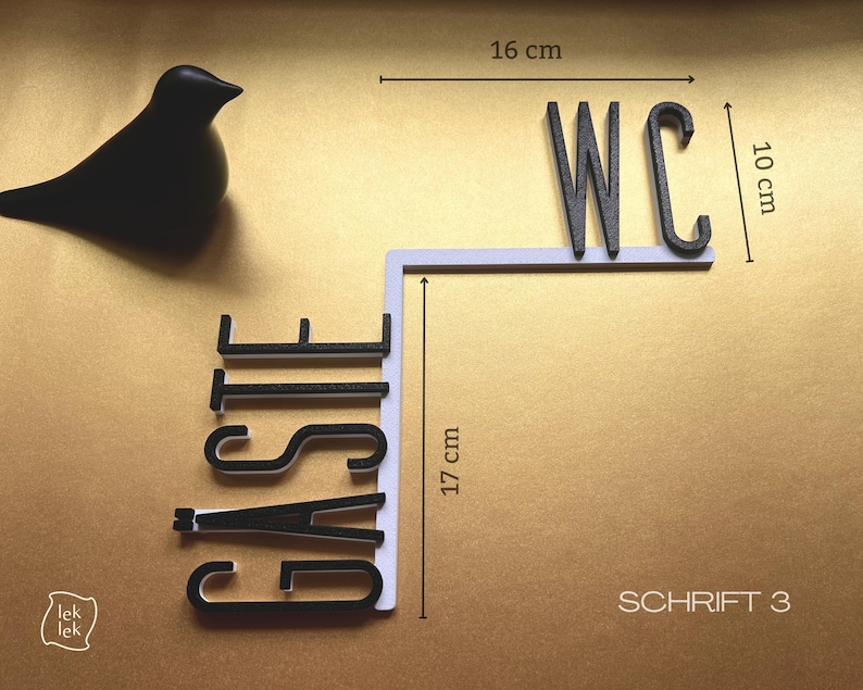 May include: A black decorative bird figurine and a black and white sign that reads "WC" (16 cm wide, 10 cm high) and "GASTE" (17 cm high). The sign is on a gold background. The text "SCHRIFT 3" is also visible.