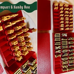 May include: A set of red plastic storage boxes containing gold-colored metal letter stamps with a gothic typeface. The text Compact & Handy Box is visible in the upper left corner. The stamps are organized in rows within the red containers.