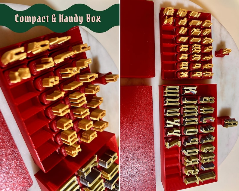 May include: A set of red plastic storage boxes containing gold-colored metal letter stamps with a gothic typeface. The text Compact & Handy Box is visible in the upper left corner. The stamps are organized in rows within the red containers.