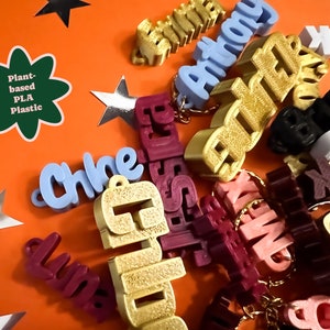 May include: A collection of personalized keychains made from plant-based PLA plastic. The keychains are in various colors, including gold, blue, red, pink, and brown. The keychains are spelled with different names, including Chloe, Anthony, Elizabeth, and Emma.