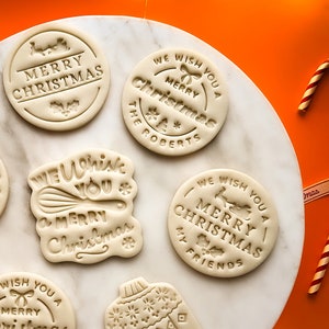 May include: A set of seven white cookie cutters with various Christmas-themed designs. The cutters feature phrases like "We Wish You a Merry Christmas" and "Merry Christmas".