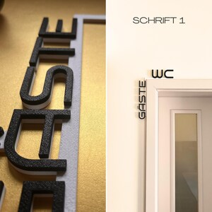 May include: Black and white 3D printed sign that says "G&auml;ste" and "WC". The sign is mounted on a white door frame. The letters are black with a white border. The background is a gold color.