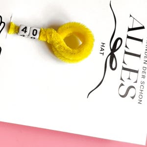 以下が含まれることがあります： ドイツ語の「ALLES」という単語と「F&Uuml;R JEMANDEN DER SCHON HAT」というフレーズが黒い筆記体で書かれた白いカード。黄色のふわふわしたパイプクリーナーが、白い文字ブロックに「40」の数字が入ったカードに付いています。