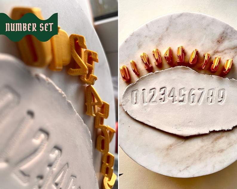 May include: A set of ten gold-colored 3D-printed number stamps from 0 to 9, arranged in a semi-circle on a white marble surface. Below the stamps, a white clay slab features the embossed sequence 0123456789. The text "NUMBER SET" is visible.