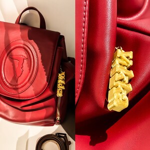 May include: A red leather backpack with a gold-colored charm that says "XOXO". The backpack has a large, embossed logo on the front.
