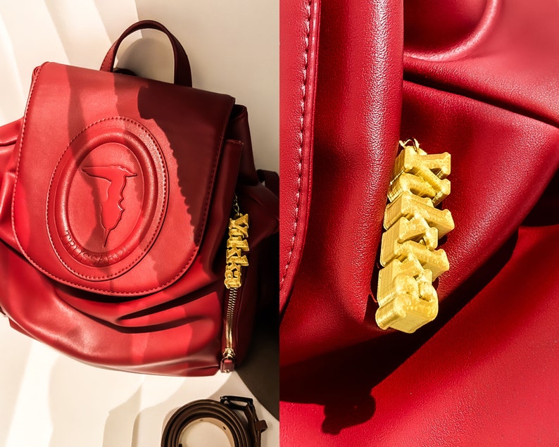 May include: A red leather backpack with a gold-colored charm that says "XOXO". The backpack has a large, embossed logo on the front.