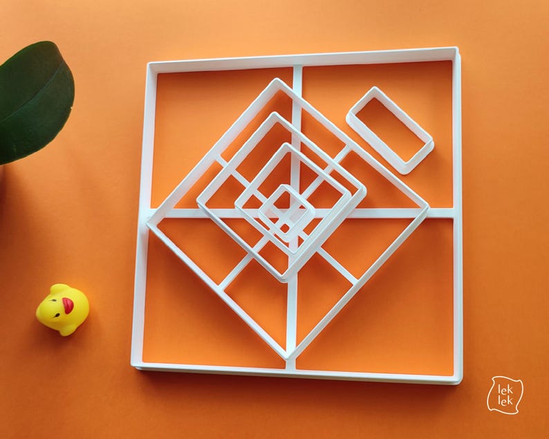 May include: White geometric cookie cutters in square and diamond shapes are arranged on an orange background. A small yellow rubber duck is in the lower left corner. The cutters are for baking and crafting.