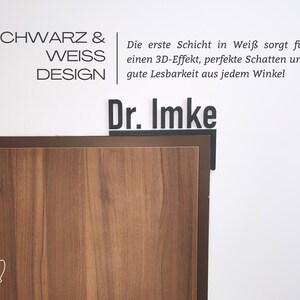 May include: A corner view of a wooden surface with the text "SCHWARZ & WEISS DESIGN" and "Dr. Imke" in black. The text "Die erste Schicht in Wei&szlig; sorgt f&uuml;r einen 3D-Effekt, perfekte Schatten und gute Lesbarkeit aus jedem Winkel" is also visible.
