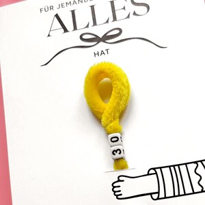 May include: A white card with the German text "F&Uuml;R JEMANDEN ALLES HAT" and a yellow question mark made of fuzzy material. The question mark has white letter beads that read "30". A cartoon hand is drawn at the bottom.