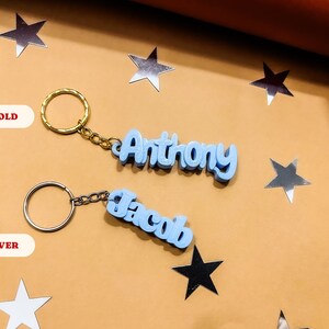 May include: Two keychains with blue plastic name tags. The keychain on the left says "Jacob" in silver and the keychain on the right says "Anthony" in gold.