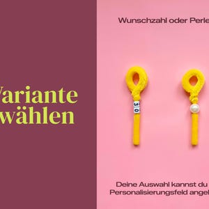以下が含まれることがあります： 「Wunschzahl oder Perle?」と「Deine Auswahl kannst du im Personalisierungsfeld angeben.」というテキストが入ったピンク色の背景。2つの黄色のモールで作られたオーナメントが表示されています。1つは数字の30、もう1つは真珠です。左側には「Variante w&auml;hlen.」というテキストがあります。