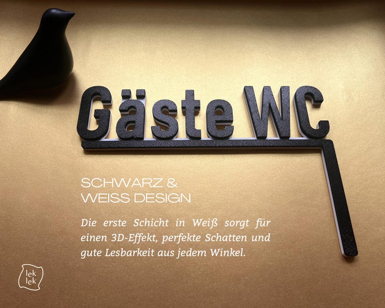 May include: Black "G&auml;ste WC" sign with white trim, and a black bird figurine on a gold background. The sign includes the text "SCHWARZ & WEISS DESIGN" and additional German text.